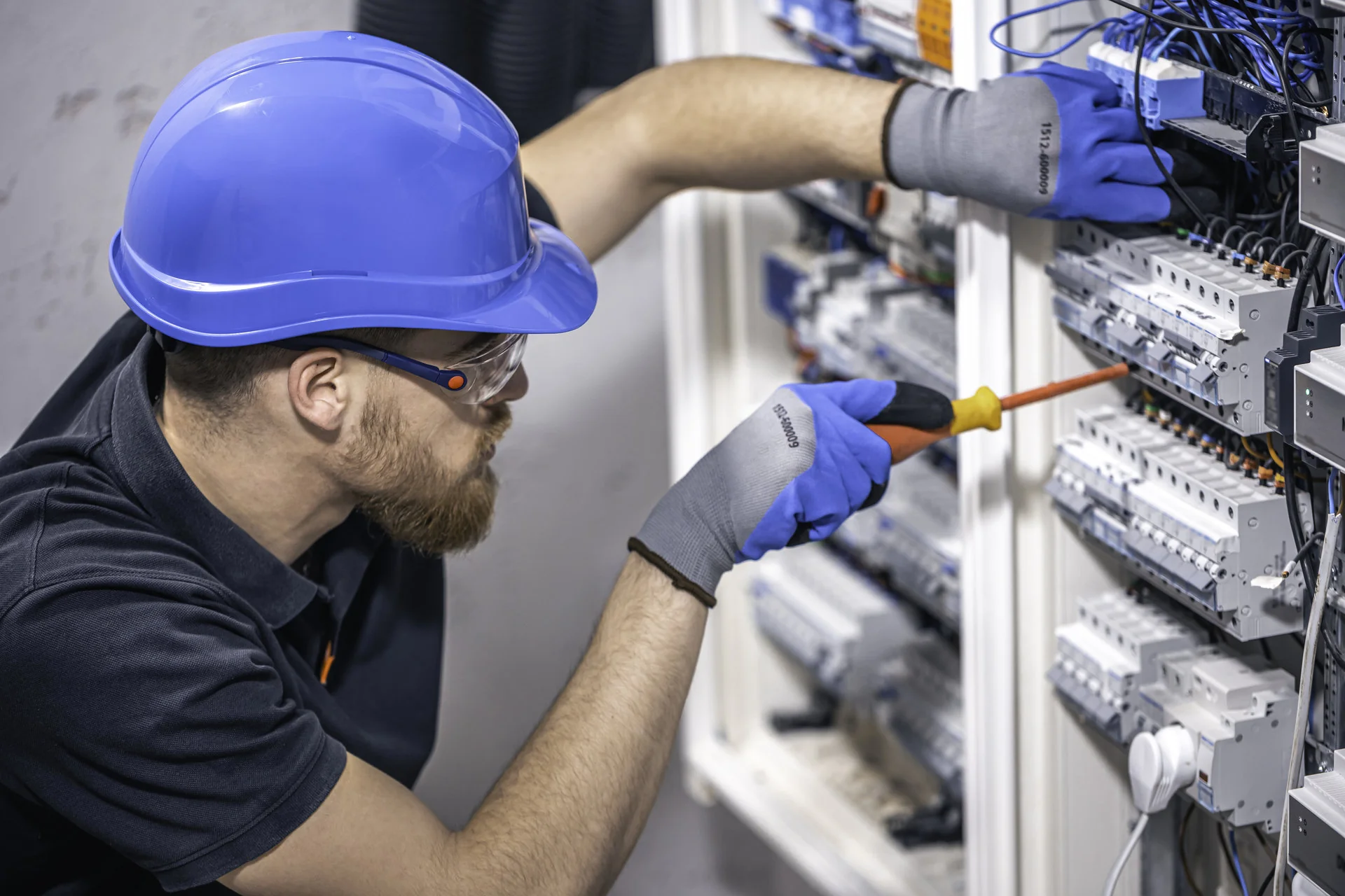 Mitarbeiter mit Schutzhelm und Schutzbrille bei Elektroarbeiten an einem Schaltschrank.